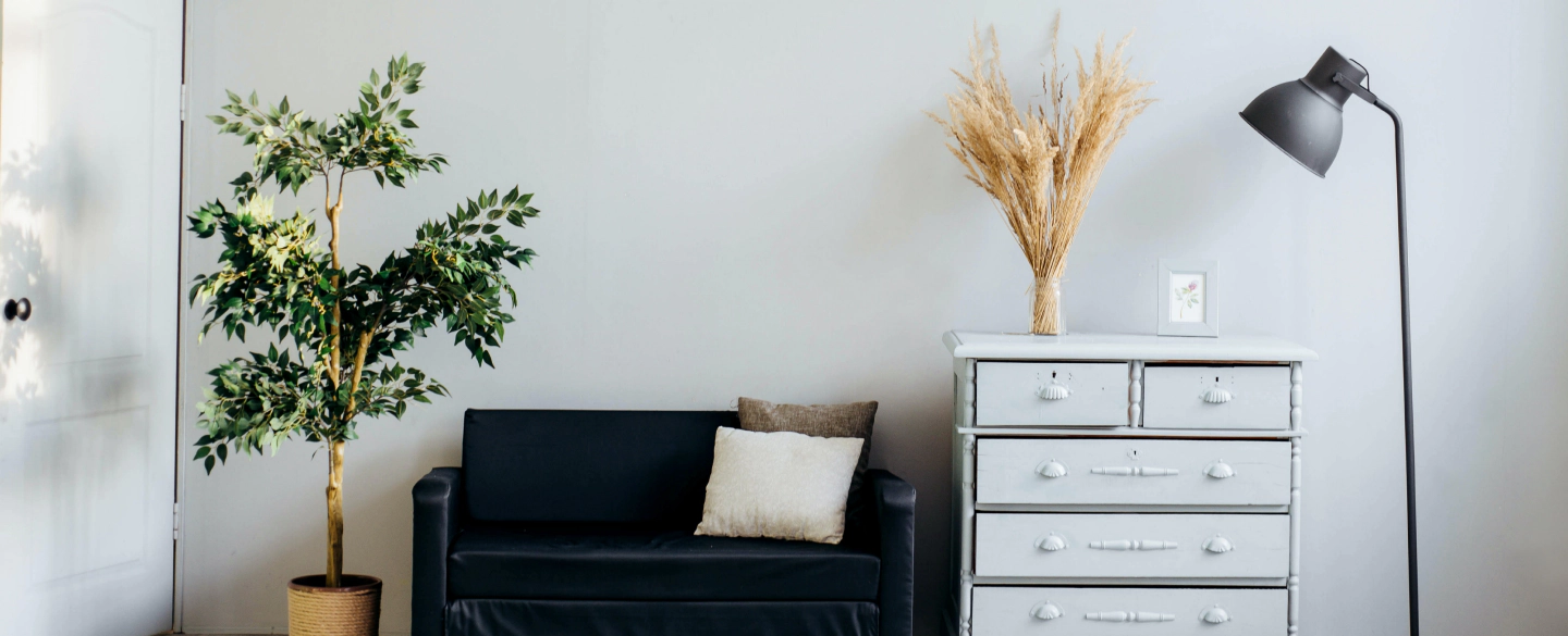 white living room with a plant a dark blue sofa a white cabinet and a grey lamp